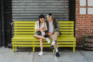 Concentrated friends sitting on bench and using smartphone